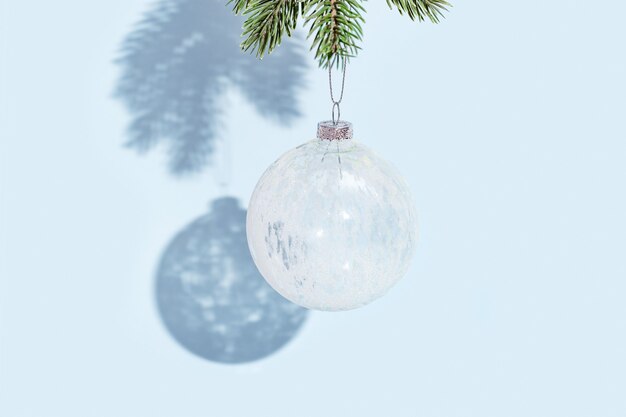 Christmas ball hanging on pine branch on blue colored wall