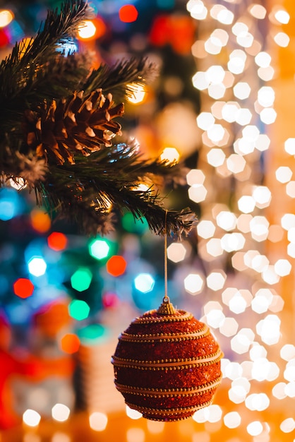 La sfera di natale appende su un abete decorato contro le luci brucianti del bokeh alla notte.