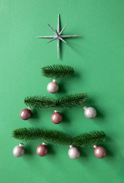 Елочные шары, декро-звезда и еловые ветки лежат в минималистичной композиции в форме елки