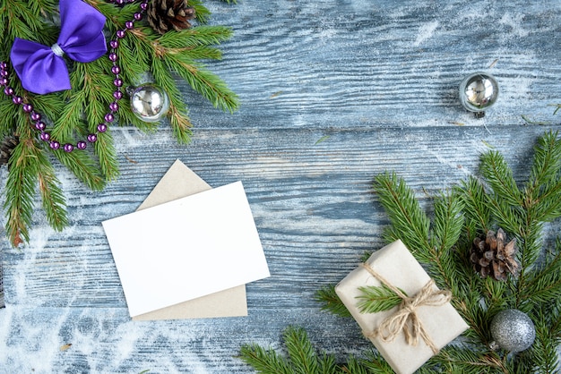 Christmas balls, fir branches, cones, purple ribbon bow, gift box and greeting envelope card on wooden surface.. Christmas decoration, copy space