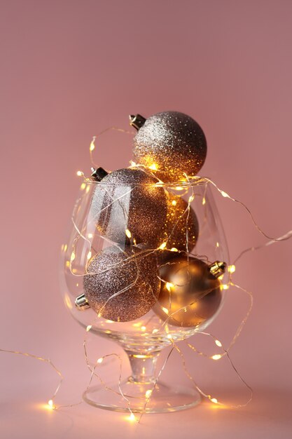 Christmas balls and garland in a glass vase on a pink background