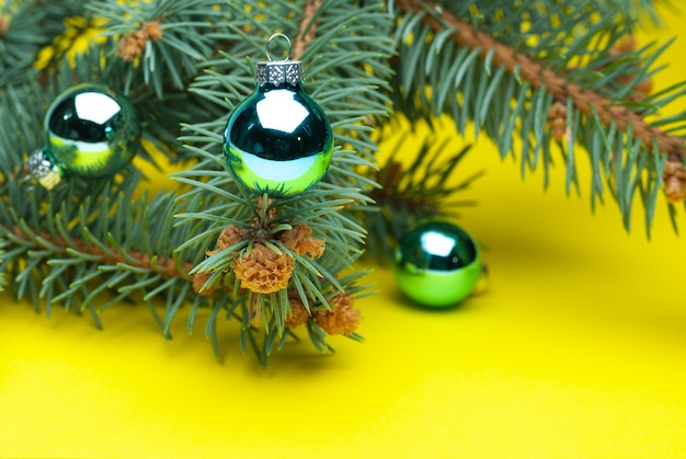黄色の背景にクリスマスボールとトウヒの枝