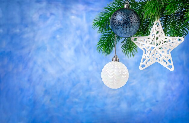 Christmas balls and star hang on fir branch on blue background