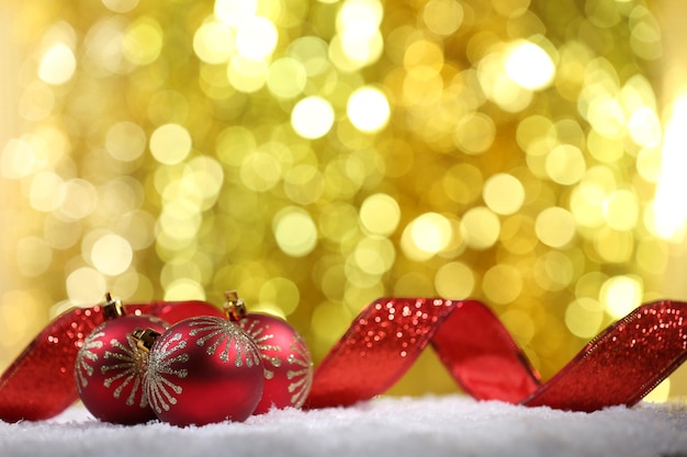 Christmas balls with red ribbon on snow on bright background