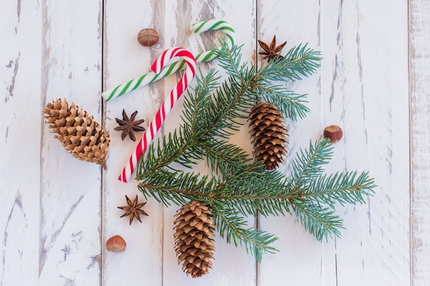 Sfondo di natale con rami di pino, coni e bastoncini di zucchero su tavole di legno rustiche.