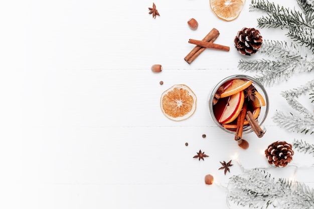 Christmas banner flat lay on white gray background with glass cup or mug of Mulled alcoholic Wine, Christmas decorations, cinnamon, orange, apple, various spices, fir, cone, anise. Conceptual photo