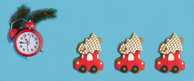 Christmas banner Red alarm clock and gingerbread in the shape of a car with fir on the blue background Copy space