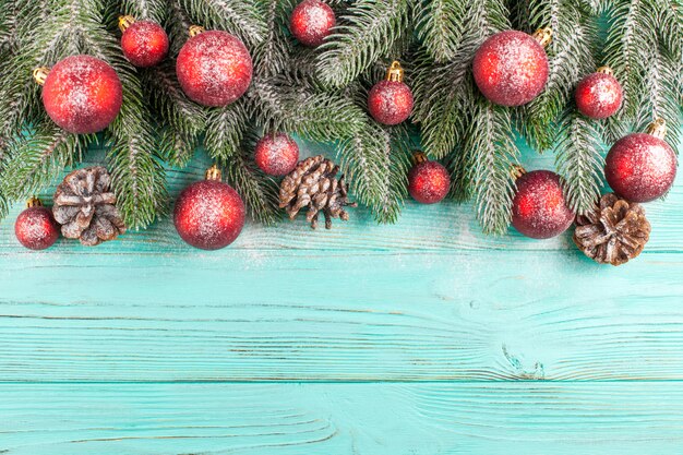 Christmas banner with green tree, red ball decorations, cones on mint wooden background under snow.