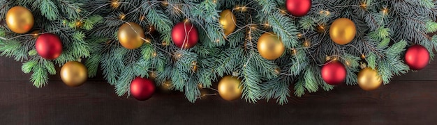 Christmas banner with natural spruce, red golden balls and a garland on a dark wooden background