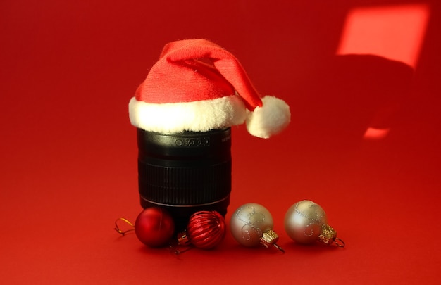빨간색에 빨간색과 흰색 크리스마스 장식이 있는 산타클로스 모자에 사진 렌즈가 있는 크리스마스 배너