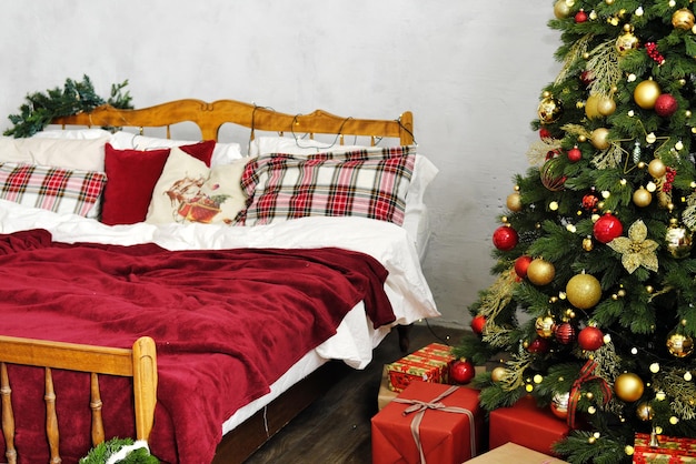 Christmas bedroom decor A large wooden bed with a red bedspread and checkered pillows and a Christmas tree in the corner of the room