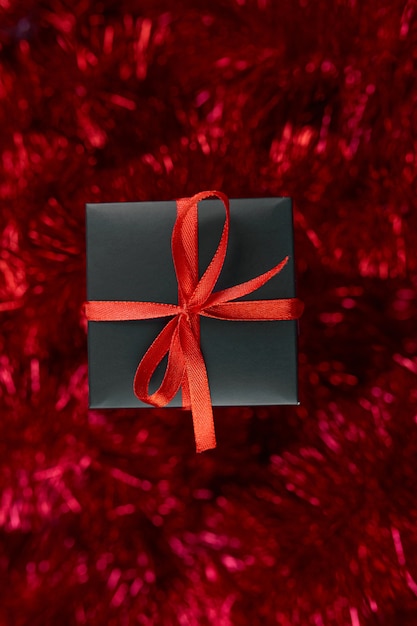 Рождественская черная подарочная коробка на фоне красной мишуры обильный декор Плоский вид сверху