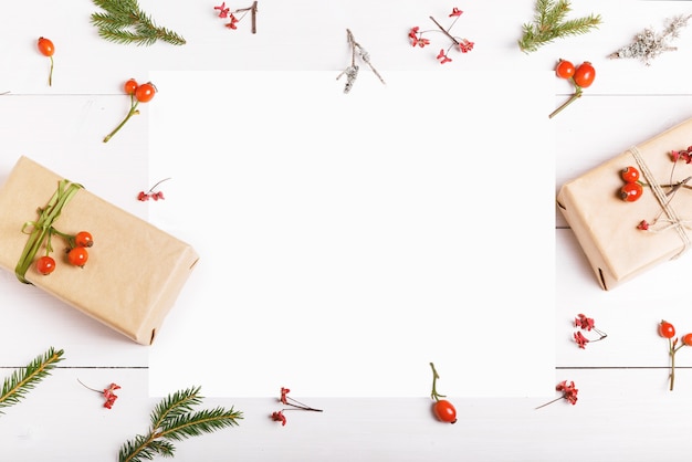 Рождественская пустая открытка в рамке из еловых веток с красными ягодами, подарочными коробками и шишками