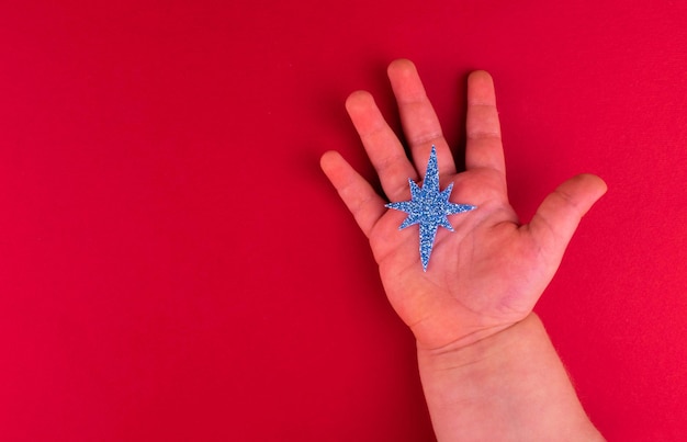 Christmas blue star in childrens hand on a red background copy space