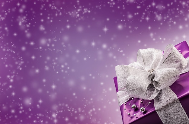 Christmas bokeh concept with purple present in the bottom right corner and illustrated snowflakes in the background.