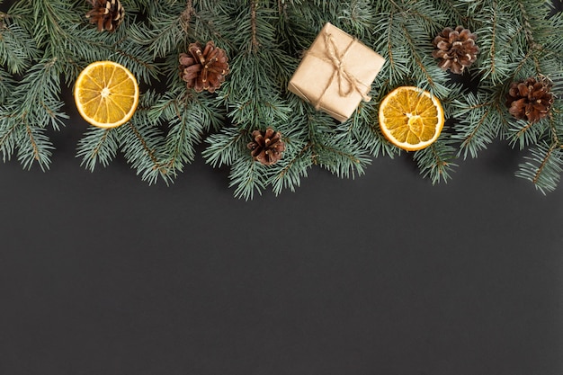 Christmas border with fir branches, cones and gift boxes on a black background.