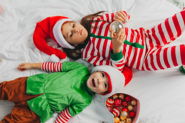 Рождество. Мальчик и девочка младшего школьного возраста лежат на полу возле украшенной елки. вид сверху