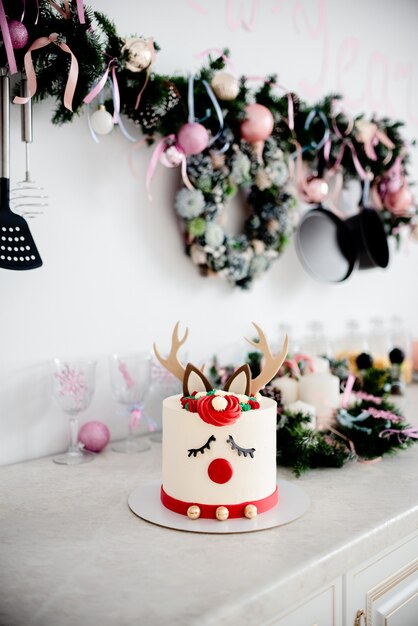 A christmas cake Deer Rudolph with red nose and christmas decorations. Decorated kitchen.