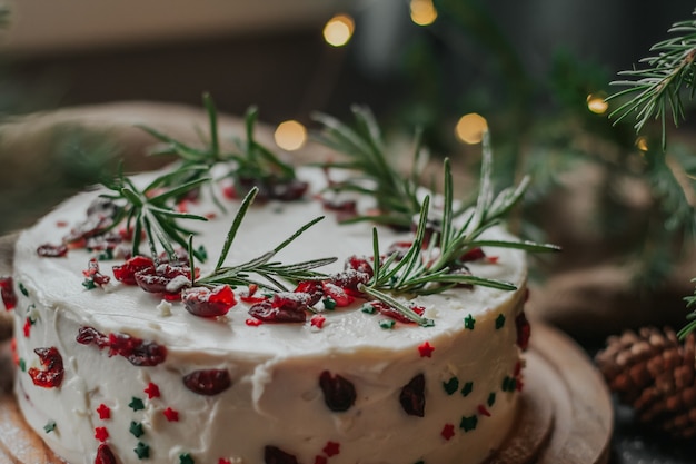 Photo christmas cake with white cheese cream, decorated with cranberries and rosemary.