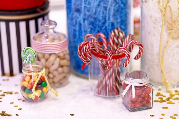 Photo christmas candy canes jars with sweets peanuts and golden confetti at the party