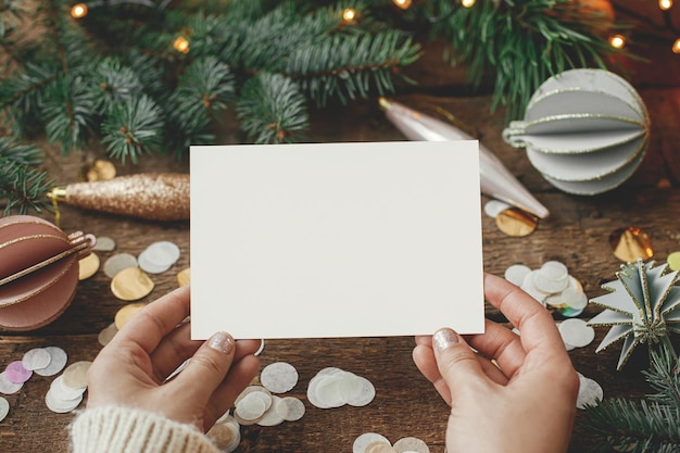 Photo christmas card mock up hands holding empty greeting card and christmas decorations confetti pine