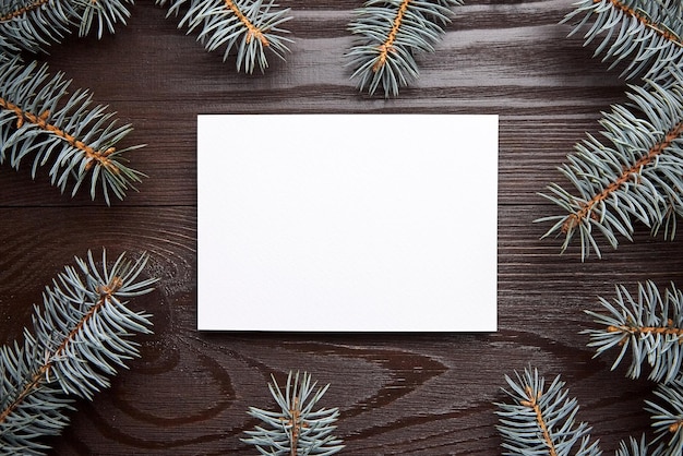 Christmas card mockup with envelope and green fir tree branches on brown wooden background top view flat lay