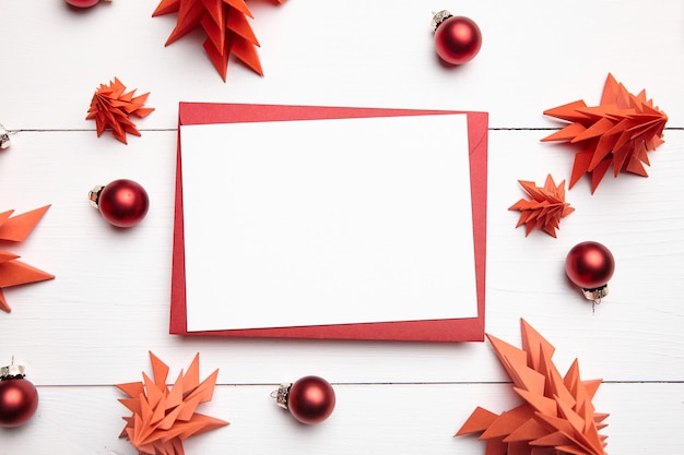 Christmas card mockup with envelope and red paper fir trees on white wooden background top view flat lay