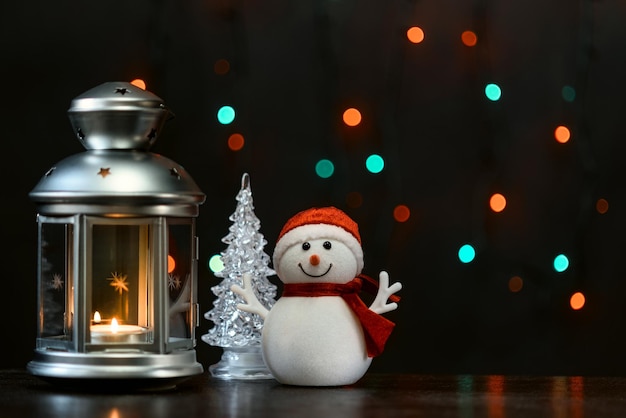 Christmas card a snowman a lantern with candles and blurry lights in the background