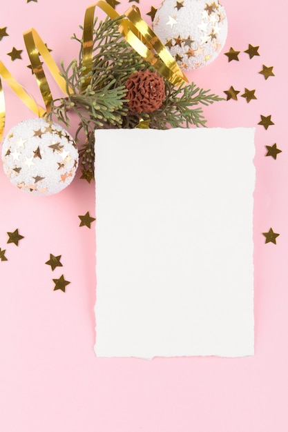 Christmas card template with fir twigs and golden stars and festive decoration on a pink pastel background.