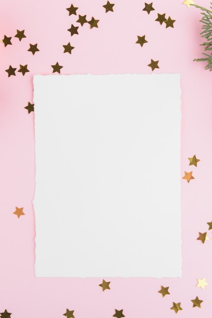 Christmas card template with fir twigs and golden stars and festive decoration on a pink pastel background.