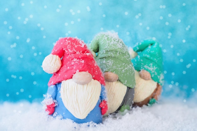 Cartolina di natale tre figure di gnomi divertenti, ricoperti di neve, si trovano una dopo l'altra su uno sfondo blu e fiocchi di neve che cadono.