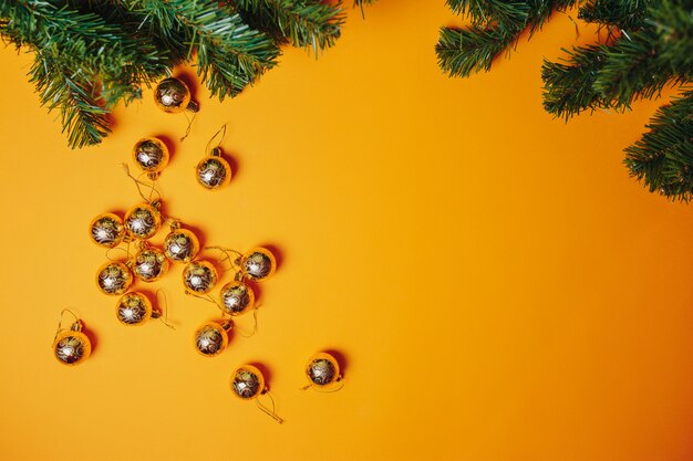 Christmas card with copyspace. Christmas ornaments flat lay on the orange . Golden balls and fir branches around.