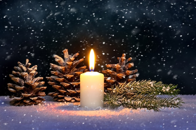 Christmas card with a lighted candle and cones during a snowfall