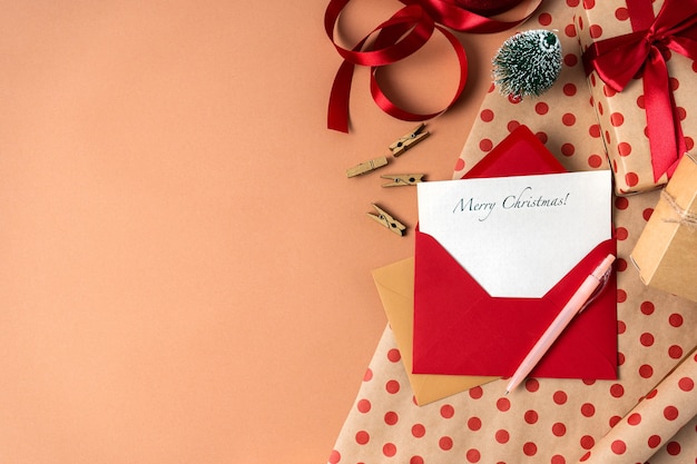 Рождественская открытка с пожеланиями в красном конверте на фоне подарочной упаковки с копией пространства