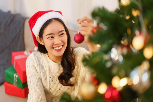 クリスマスのお祝いのコンセプト クリスマス ツリーで飾るために赤いボールを保持している若いアジア女性