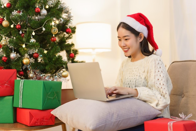 크리스마스 축하 개념 산타 모자를 쓰고 노트북으로 온라인 쇼핑을 하는 젊은 아시아 여성