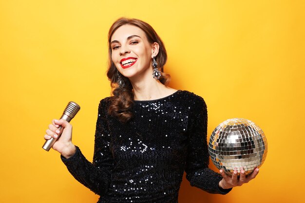 Christmas celebration party holiday concept Young woman in evening dress holding microphone and disco ball