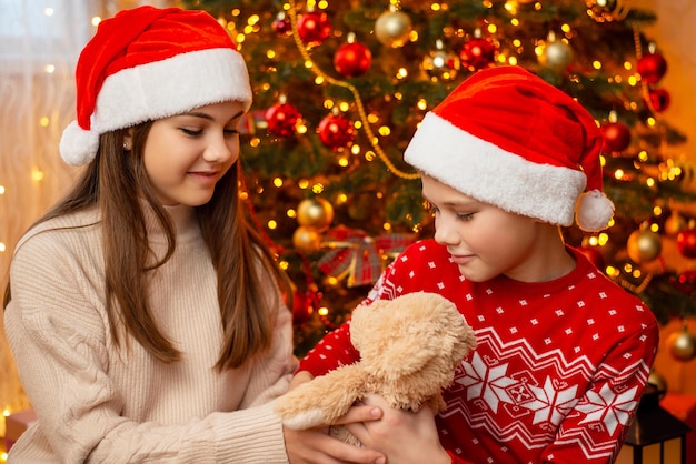 Christmas child girl giving teddy bear to younger brother