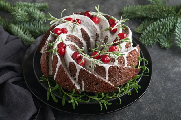 Christmas chocolate bundt cake Traditional Christmas fruit cake with white glaze cranberries and rosemary on dark backgroundChristmas decoration Winter baking at Xmas or New Year Copy space