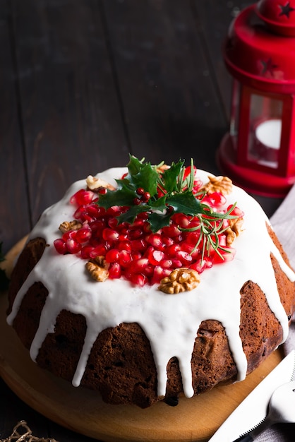 Christmas chocolate cake with white icing and pomegranate kernels on a wooden dark  with red lantern and poinsettia