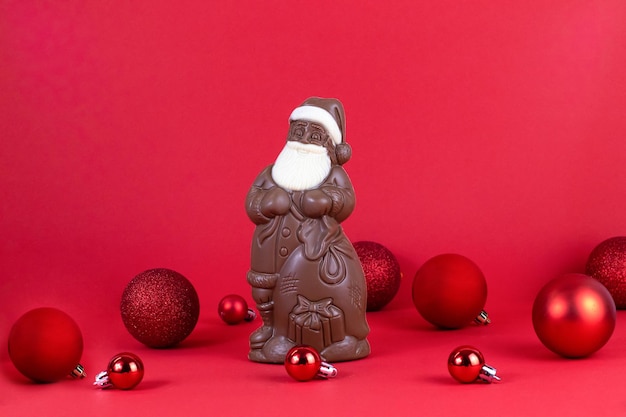 Рождество. Шоколадный Санта-Клаус на красном фоне, воздушный шар. Место для текста, праздника, подарков,