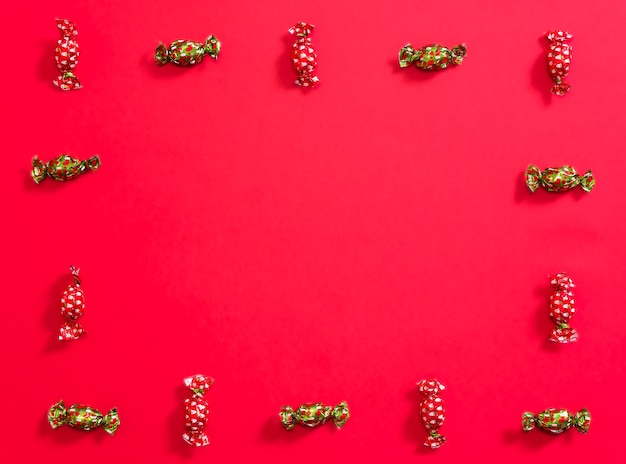 Christmas chocolates placed forming a frame on a red background alternating chocolates with red and green wrapping