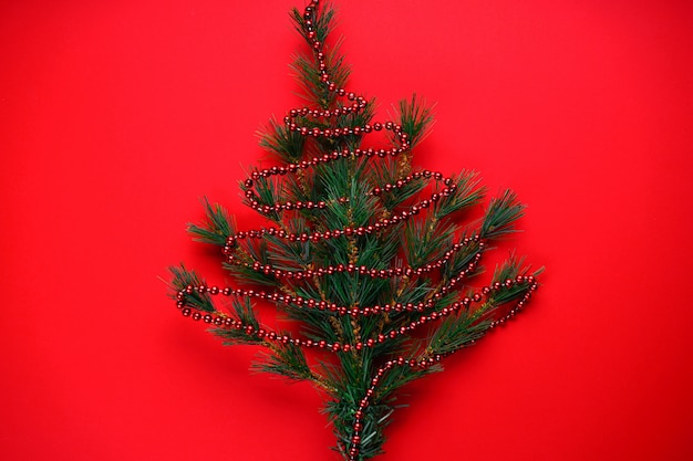 Foto natale o addobbi natalizi: rami di un albero di natale a forma di albero di natale con perline rosse su fondo rosso