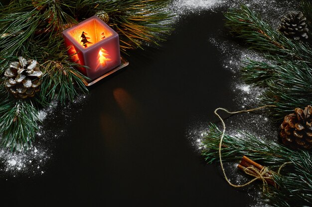 Christmas, christmas tree, candle, snow, cones and cinnamon sticks on black background. Top view. Copy space. Still life. Flat lay New year