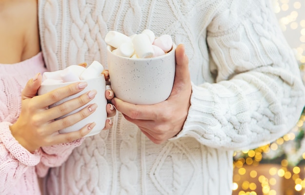 Christmas cocoa with marshmallows in the hands of a man and a woman. Selective focus.