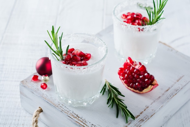 Christmas coconut punch with pomegranate seeds and sprigs of rosemary on light surface