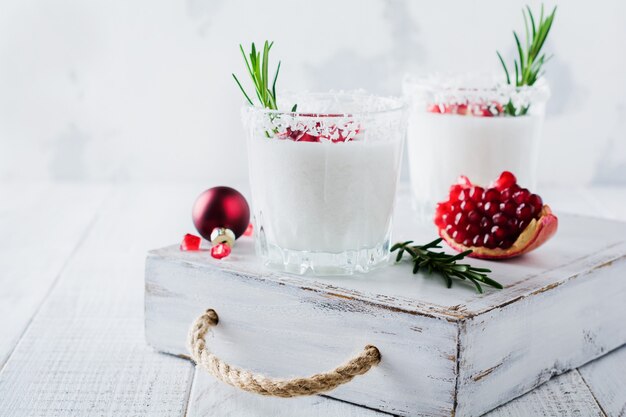 Christmas coconut punch with pomegranate seeds and sprigs of rosemary on light surface