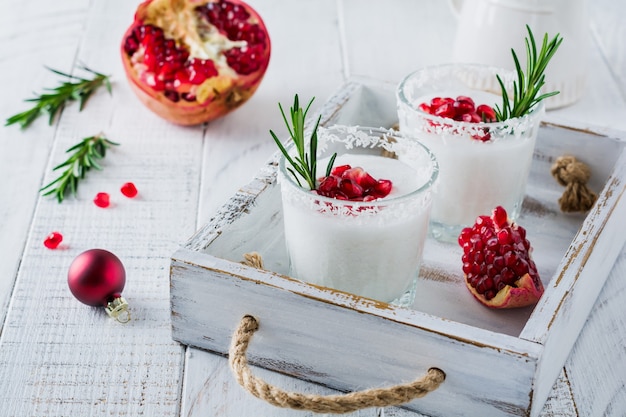 Christmas coconut punch with pomegranate seeds and sprigs of rosemary on light surface