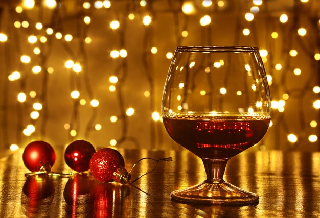 Photo christmas colorful balls and glass cognac or whiskey with defocused lights