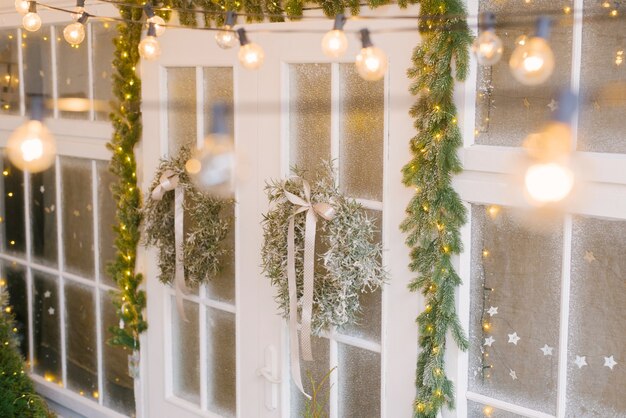 Christmas comfort. Christmas tree wreaths on white doors surrounded by numerous lights